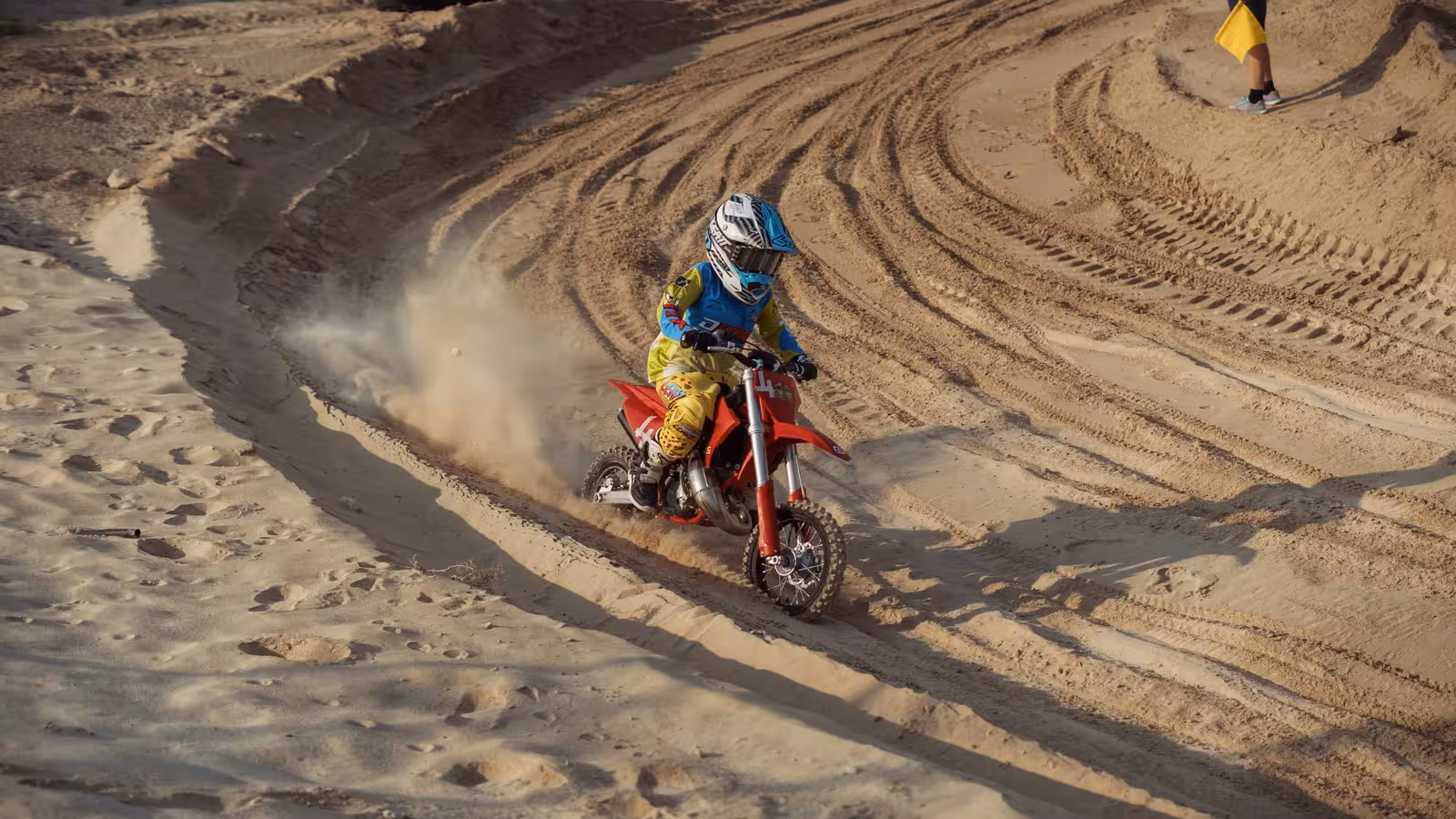 Motocross rider, number 23, on a white and blue dirt bike creating a large dust cloud while racing on a sandy DMX track.