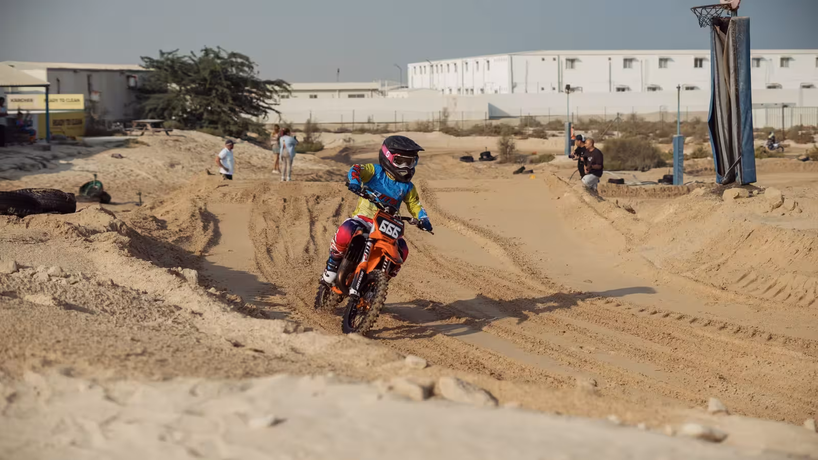Young motocross rider on a red dirt bike kicking up dust while cornering on a sandy DMX race track.