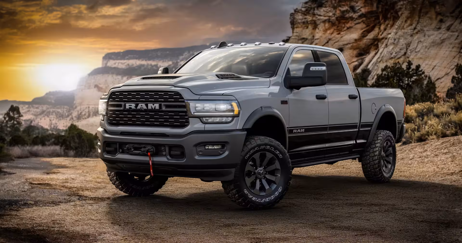 Front three-quarter view of the 2026 Ram 2500 Power Wagon Lunar Edition in Ceramic Grey with black lower body and black wheels, featuring a front winch and aggressive off-road tires, parked on a dirt road at sunset.