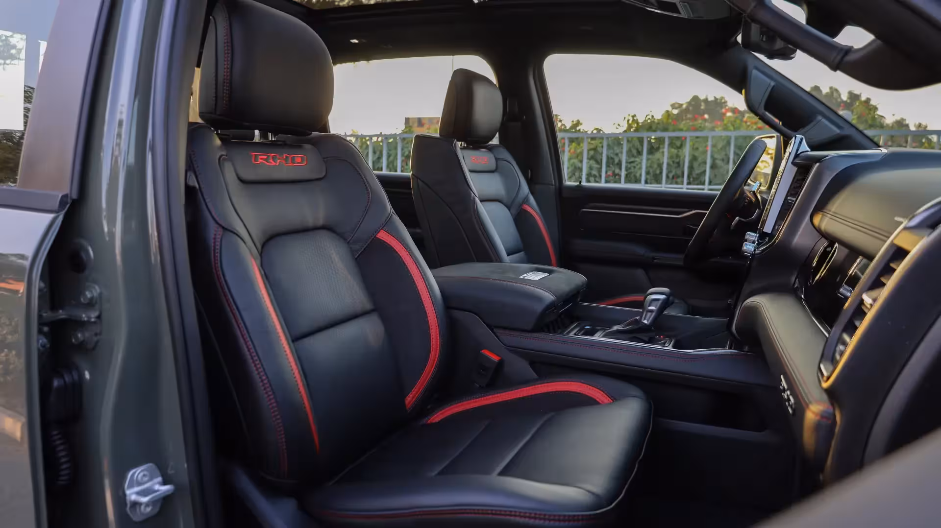 Interior view of the 2026 Ram 1500 RHO, showing black leather and suede front seats with red stitching and 'RHO' embroidery on the seatbacks, and a panoramic sunroof.