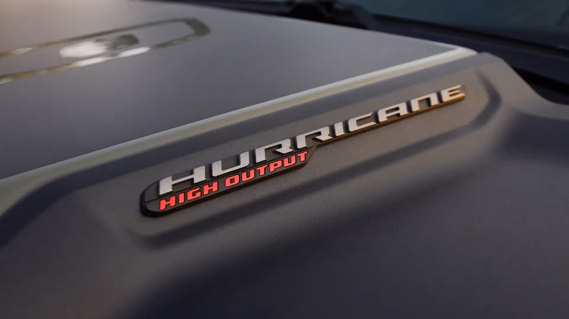 Close-up of the 'RHO' badge in dark grey on the olive green body of the 2026 Ram 1500 RHO, with a portion of the taillight visible.