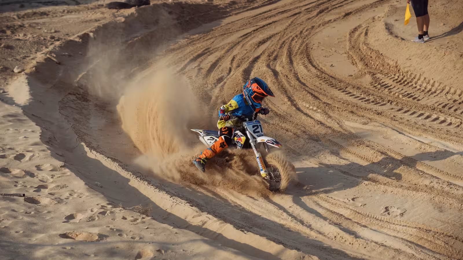 Motocross rider, number 2, on a blue and white dirt bike with blue rims, leaning into a dusty turn on the DMX track.