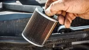 Pair of hands holding a shiny, new or reconditioned car alternator with its pulley and copper windings, in a dark garage setting.