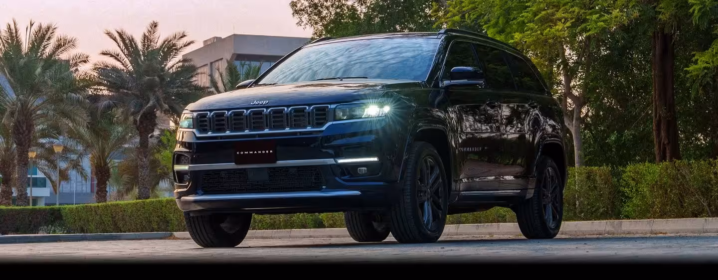 A light silver Jeep Commander SUV with black multi-spoke wheels confidently climbing a steep, rocky off-road incline, showcasing its legendary 4x4 capability.