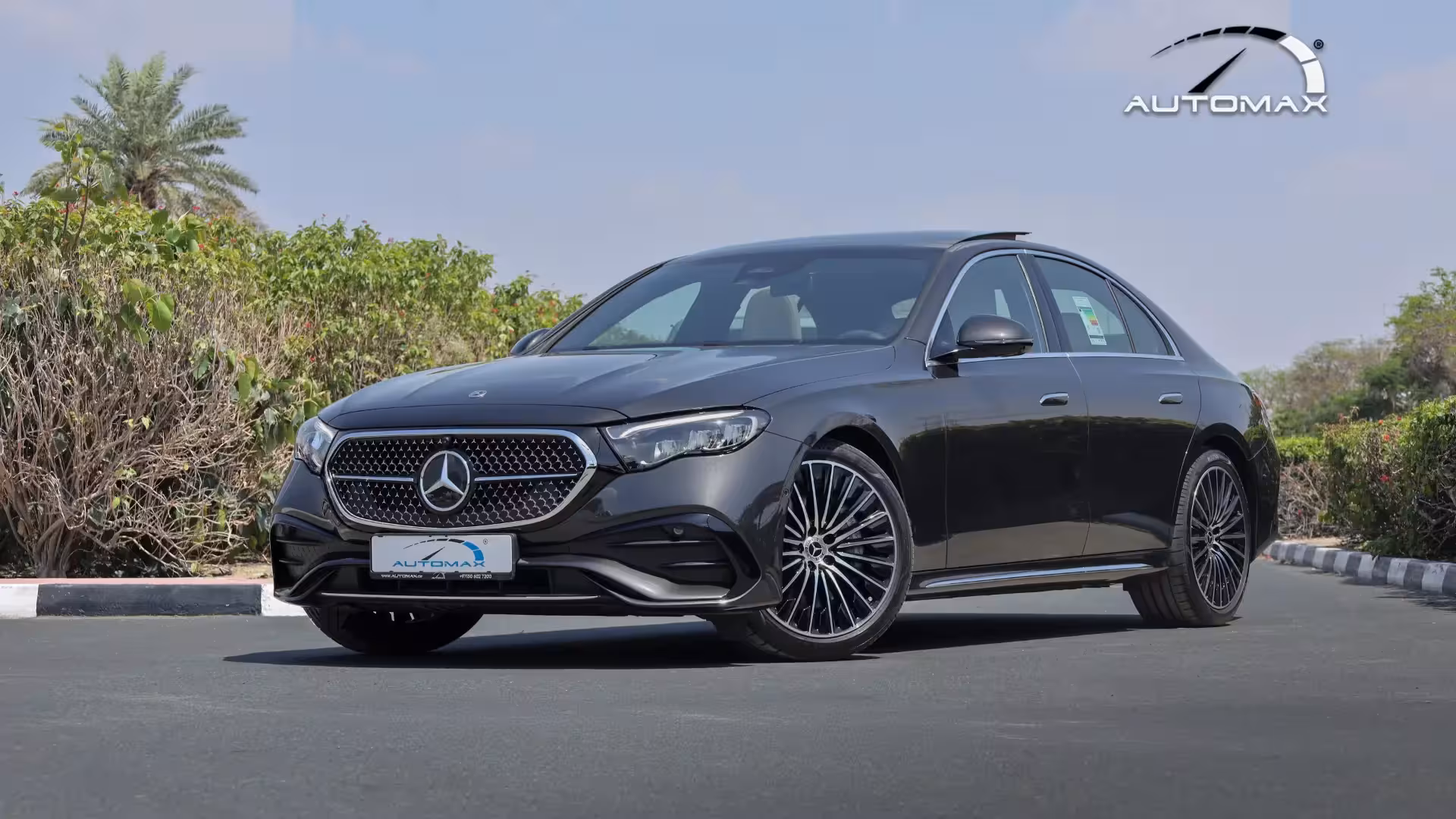 Front three-quarter view of the 2026 Mercedes-Benz E 200 AMG in black, showcasing its distinctive grille with integrated Mercedes stars, sharp LED headlights, and AMG-styled bumper.