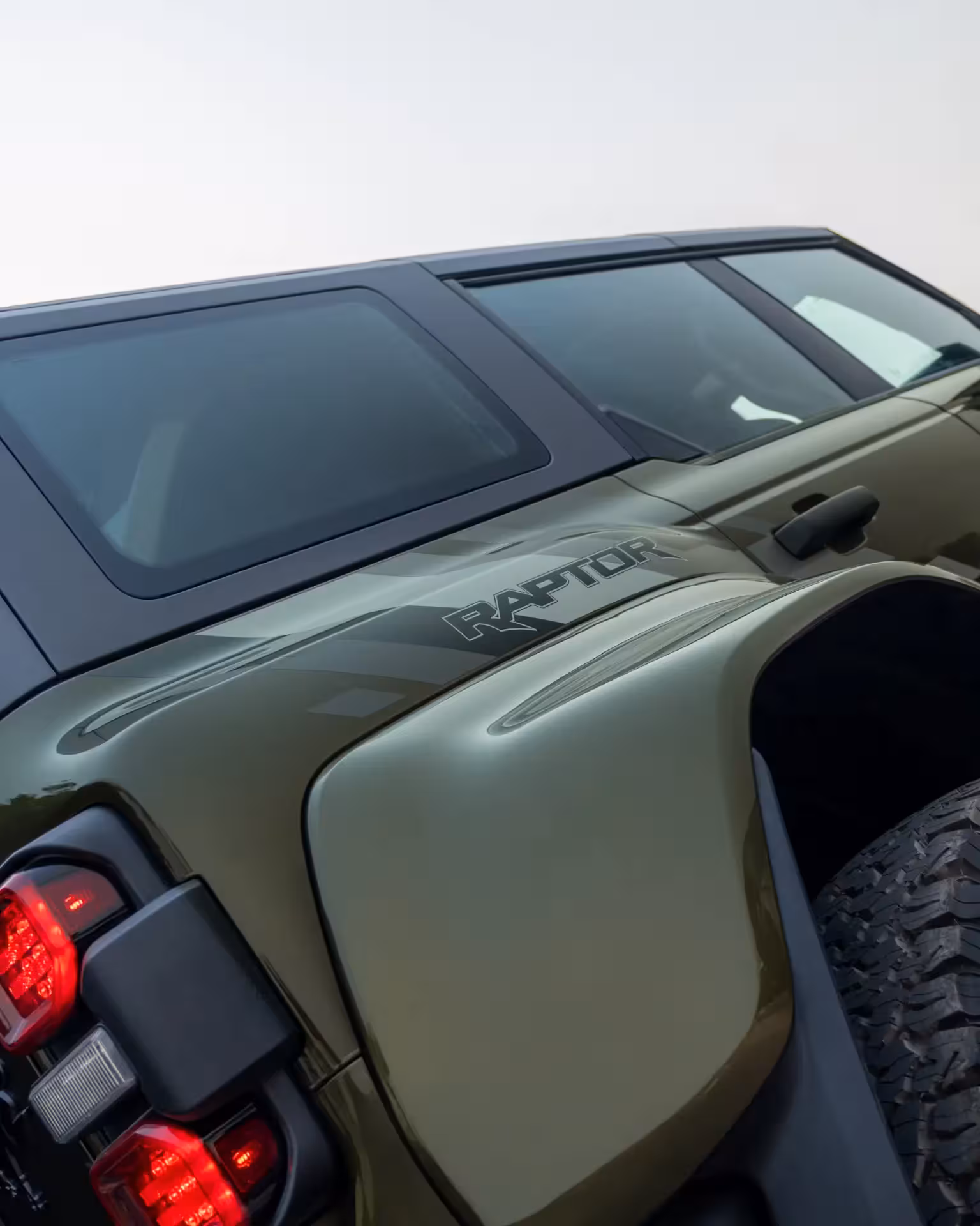 Rear three-quarter view of a dark green/khaki 2025 Ford Bronco Raptor, showing the 'RAPTOR' decal on the fender and aggressive wheel arches.