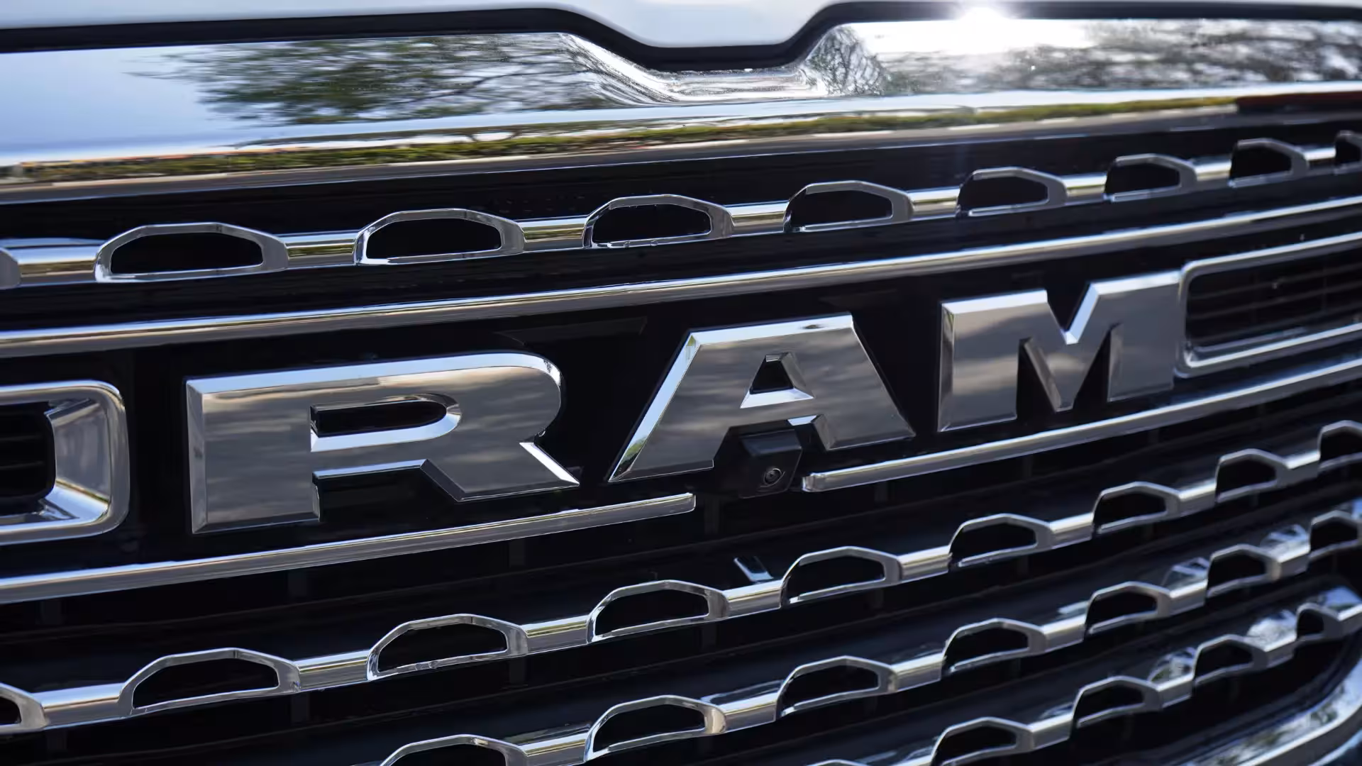 Close-up of the bold chrome front grille of the 2026 Ram 1500 Longhorn, showing the 'RAM' lettering and an integrated front camera.