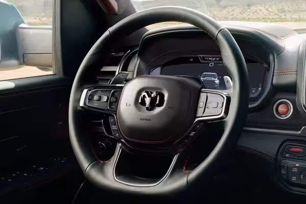 Close-up of the leather and carbon-wrapped flat-bottom steering wheel of the 2027 Ram TRX, featuring red stitching, integrated aluminum paddle shifters, and the Ram logo.