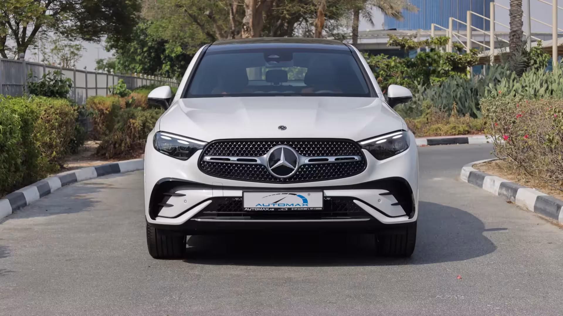 Dynamic low-angle front three-quarter view of a black 2026 Mercedes-Benz GLC 200 Coupe on a paved road with lush green bushes in the background, highlighting its sleek lines and powerful stance.