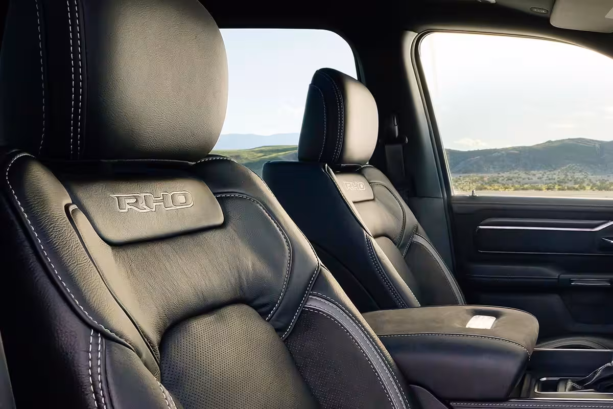 Close-up of luxurious black leather car seats with white contrast stitching and 'RHO' embossed on the headrest, featuring intricate padding.