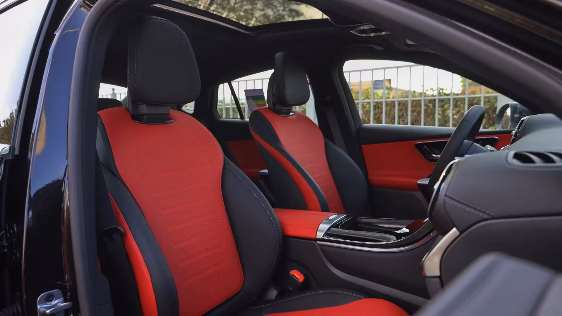 Interior view of the 2026 Mercedes-Benz GLC 200 Coupe, showing the front driver and passenger seats upholstered in a striking red and black two-tone design, with a panoramic sunroof visible overhead.