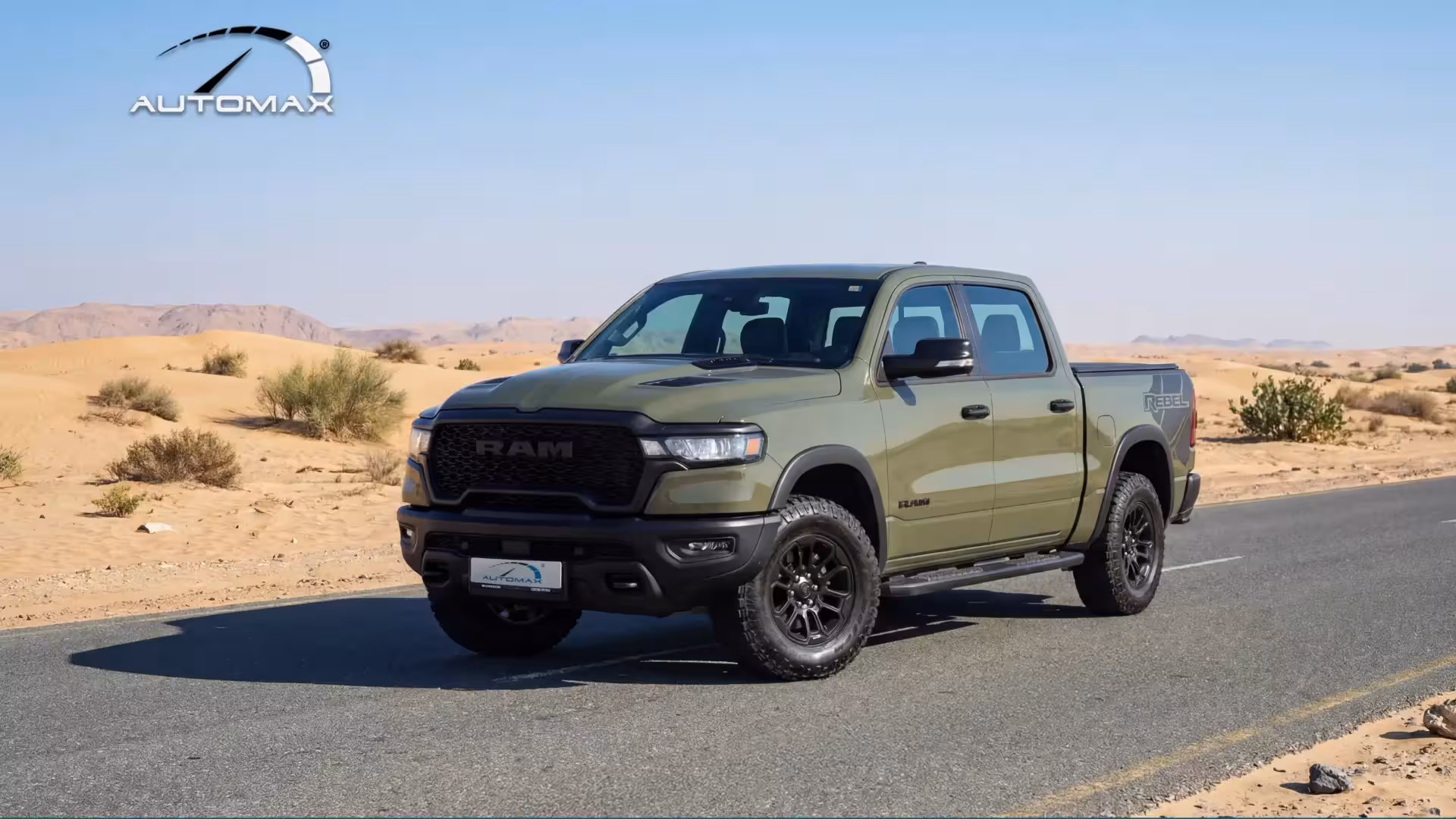 Front three-quarter view of a dark gray 2026 Ram 1500 Rebel parked on a rooftop lot with puddles, emphasizing its aggressive stance and blacked-out features.