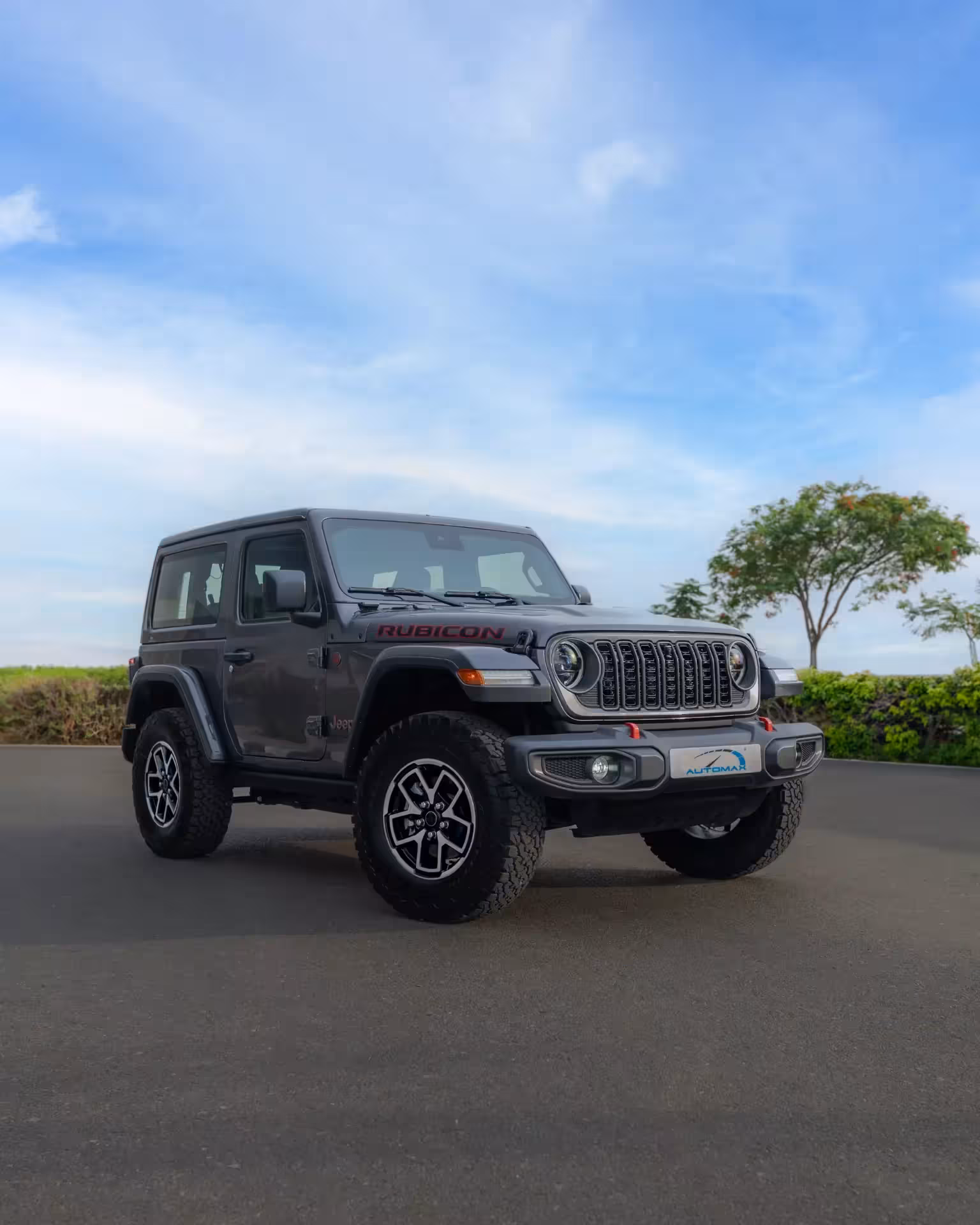 Front left view of a dark gray two-door Jeep Wrangler Rubicon parked on asphalt under a blue sky.