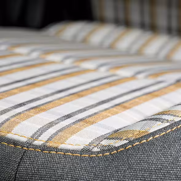 Close-up of the plaid interior fabric of a Jeep 85th Anniversary Special Edition seat, showing white, grey, and gold stripes with Mayan Gold stitching.