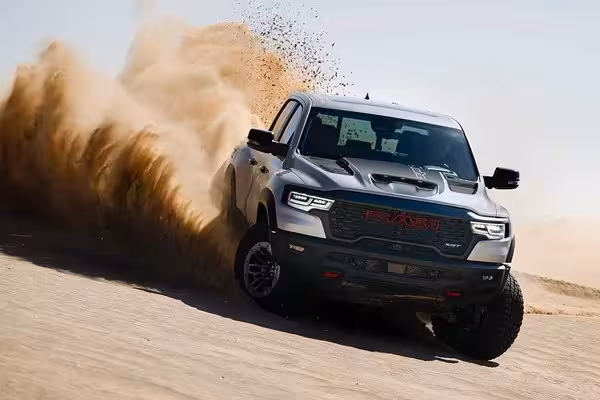 Wide interior shot of the 2027 Ram TRX cabin, showcasing the large 14.5-inch Uconnect touchscreen, flat-bottom steering wheel, and luxurious front seats with red stitching. An off-road landscape is visible through the windshield.