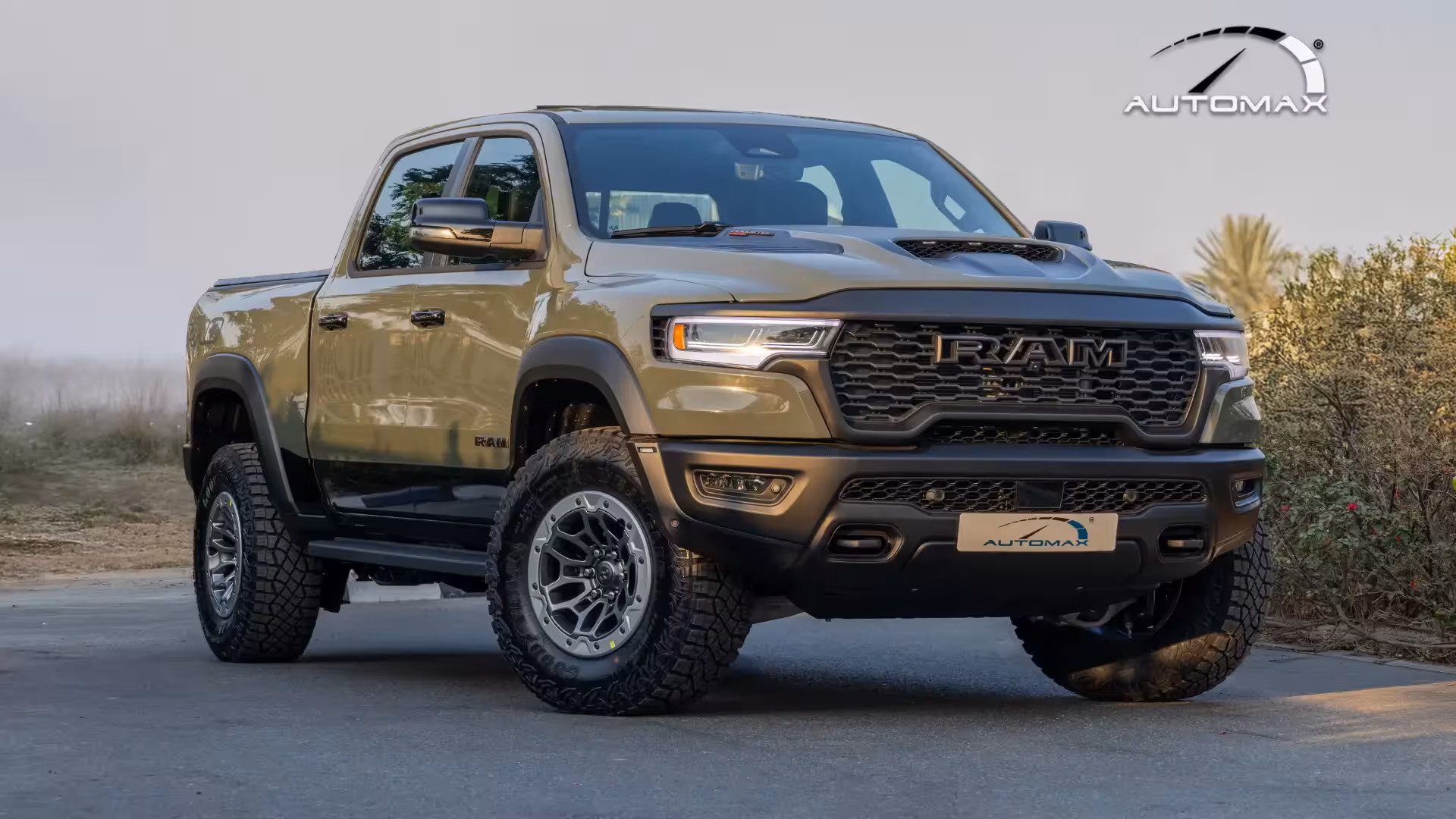 Front three-quarter view of the 2026 Ram 1500 RHO in olive green, showcasing its wide stance, prominent RAM grille, and large off-road tires.
