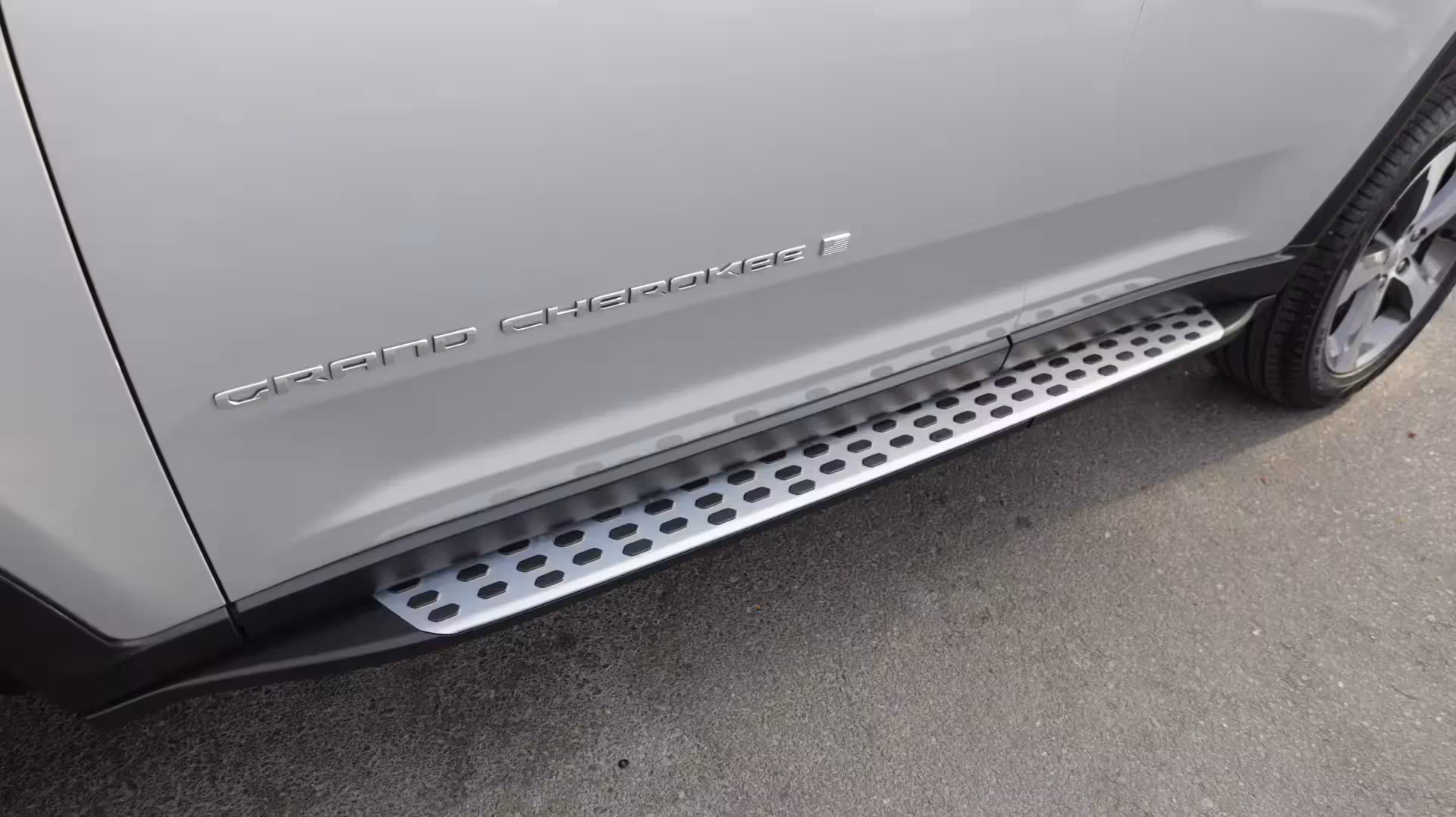 Close-up of the 'GRAND CHEROKEE' badge with an American flag emblem on the side of a silver 2025 Jeep Grand Cherokee.