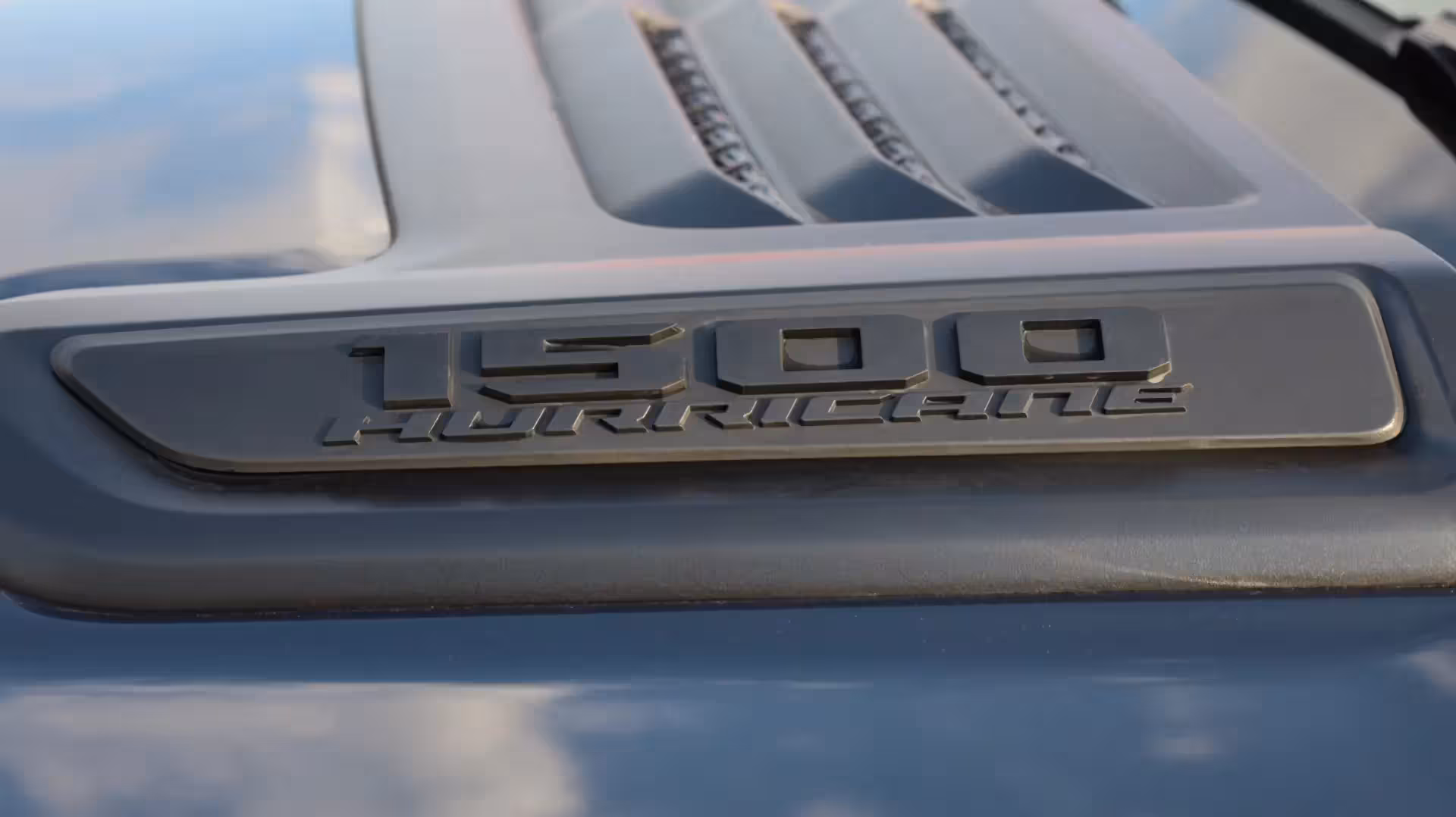Close-up of the '1500 HURRICANE' badge on the hood of a dark gray Ram 1500, with hood vents visible.
